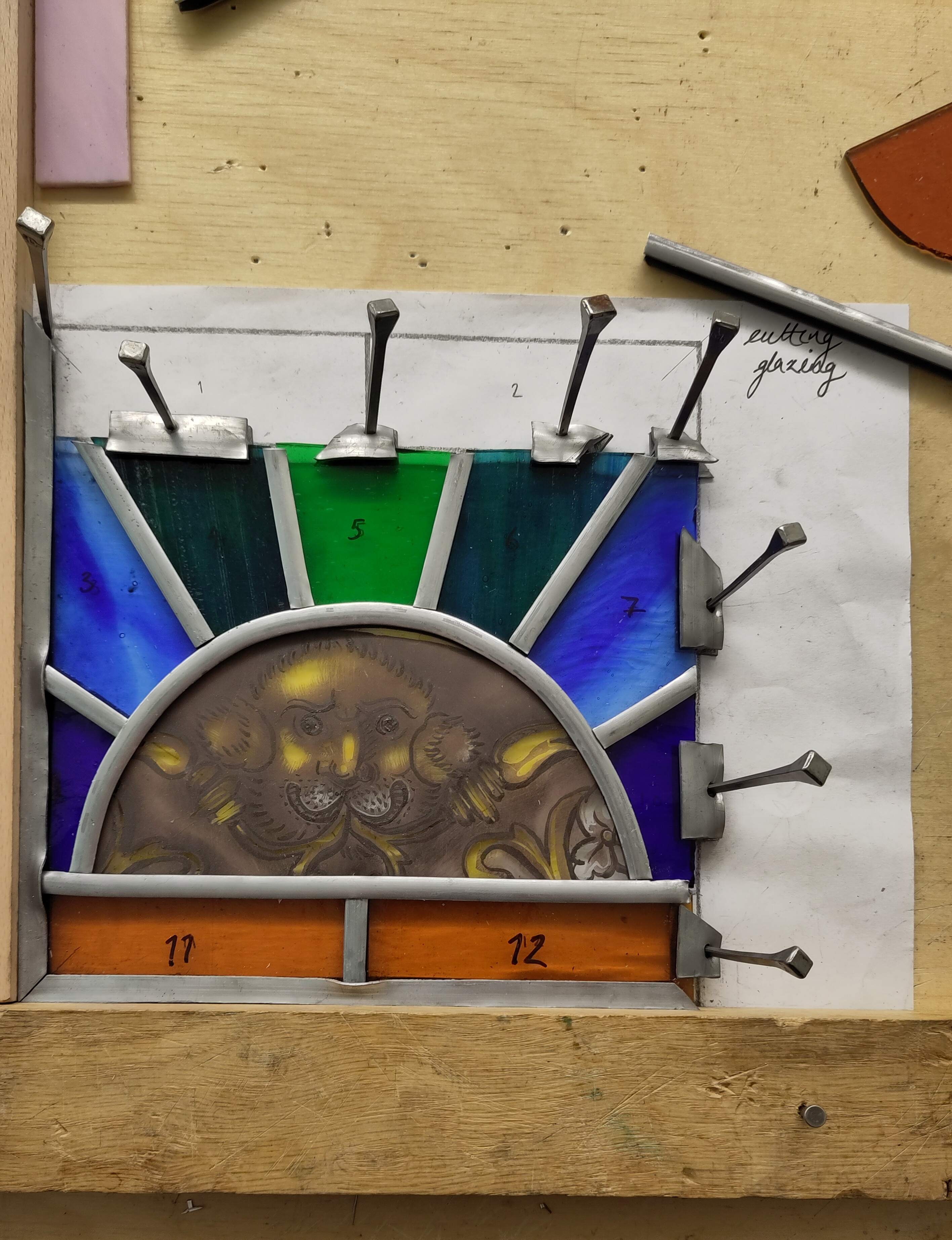 An image of the glazing process. Lead came is being fit in between the glass pieces and the panel is held together with wooden planks and nails.